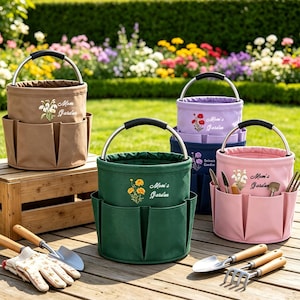 Op de afbeelding: Vier cilindervormige tuingereedschapstassen van canvas in beige, donkergroen, lichtpaars en roze, elk voorzien van een metalen handvat, buitenzakken en geborduurde bloemmotieven met de tekst Mom's Garden. Tuingereedschap ligt in de buurt.