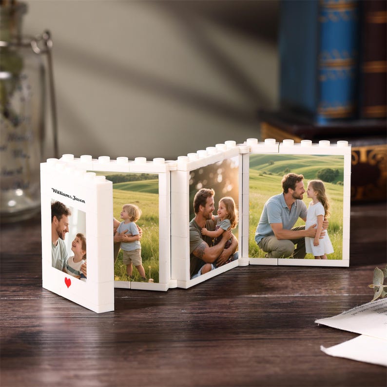 May include: A white, modular, brick-style folding picture frame featuring three connected panels. The frame displays photographs of a family in a grassy field. The front panel includes the text "Williams, Jason" and a small red heart icon.