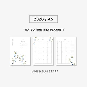 Puede incluir: Un planificador mensual fechado blanco para 2026 en tamaño A5. El planificador incluye un calendario de julio y una vista mensual. Elementos botánicos decorativos con bayas azules y hojas verdes adornan las páginas. También se ve el texto "MON & SUN START".
