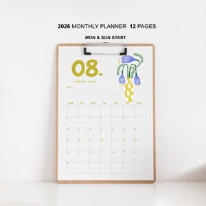 May include: A 2026 monthly planner with 12 pages, starting on Monday and Sunday. The August page features a yellow "08" and floral illustration. The calendar is held by a wooden clipboard.