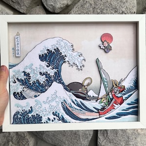 May include: Framed artwork showing a stylized wave scene with a boat and characters. The artwork has a white frame and a colourful illustration with Japanese text. The characters are in a boat, and a figure with a red sun is in the upper right corner.