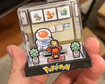 Könnte beinhalten: Ein Miniatur-Diorama mit einer Szene aus der Pokémon-Videospielserie. Die Szene zeigt einen Trainer, Pokémon und das Pokémon-Logo. Das Diorama ist in einer transparenten, rechteckigen Box eingeschlossen.