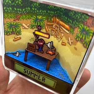 May include: A 3D diorama featuring a pixelated summer scene. A figure stands on a wooden dock with a seagull and crab. The scene includes a sandy beach, ocean, and lush green foliage. The word "SUMMER" is displayed.