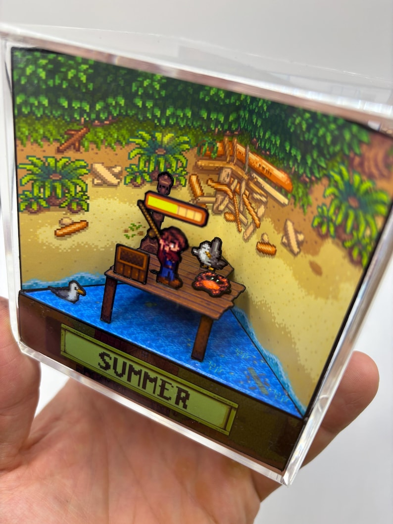 May include: A 3D diorama featuring a pixelated summer scene. A figure stands on a wooden dock with a seagull and crab. The scene includes a sandy beach, ocean, and lush green foliage. The word "SUMMER" is displayed.
