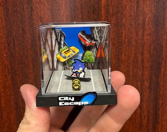 May include: A miniature diorama featuring Sonic the Hedgehog on a skateboard, with the words "City Escape" on the base. The scene includes a road, buildings, and miniature cars. The diorama is encased in a clear box.