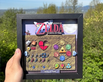 May include: A framed artwork featuring the "Legend of Zelda: Ocarina of Time" game interface. The artwork includes the game's logo, quest status, heart containers, and musical notes. The frame is black, and the background shows a scenic view.