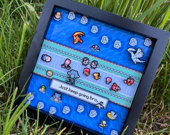 Puede incluir: Una obra de arte enmarcada con un diseño pixelado, con un fondo de agua azul y varios personajes coloridos. El texto "Just keep going bro." se muestra en una pancarta blanca. El marco es negro.