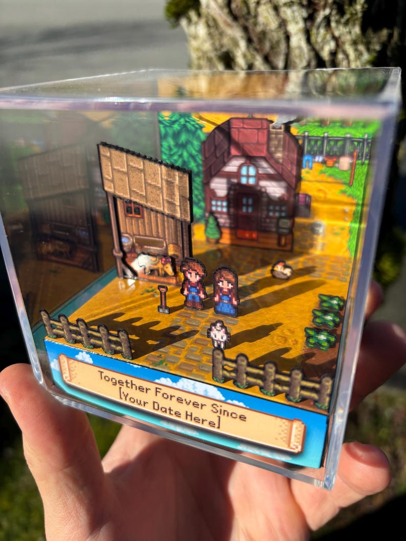May include: A miniature diorama in a clear acrylic box depicts a pixelated farm scene. Two figures stand near a house and barn, with a fence and crops in the foreground. Text on the base reads "Together Forever Since [Your Date Here]."