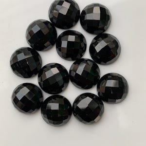May include: A collection of twelve faceted, round, black gemstones. Each gem has a multi-faceted surface that reflects light, creating a sparkling effect. The gems are arranged on a white surface.