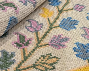 Könnte beinhalten: Nahaufnahme eines beigefarbenen Teppichs mit floralem Muster. Das Design zeigt stilisierte Blumen in Blau-, Rosa- und Gelbtönen mit grünen Stielen. Ein gelber Rand verläuft entlang der Kante. Der Teppich ist teilweise aufgerollt und zeigt die Rückseite.