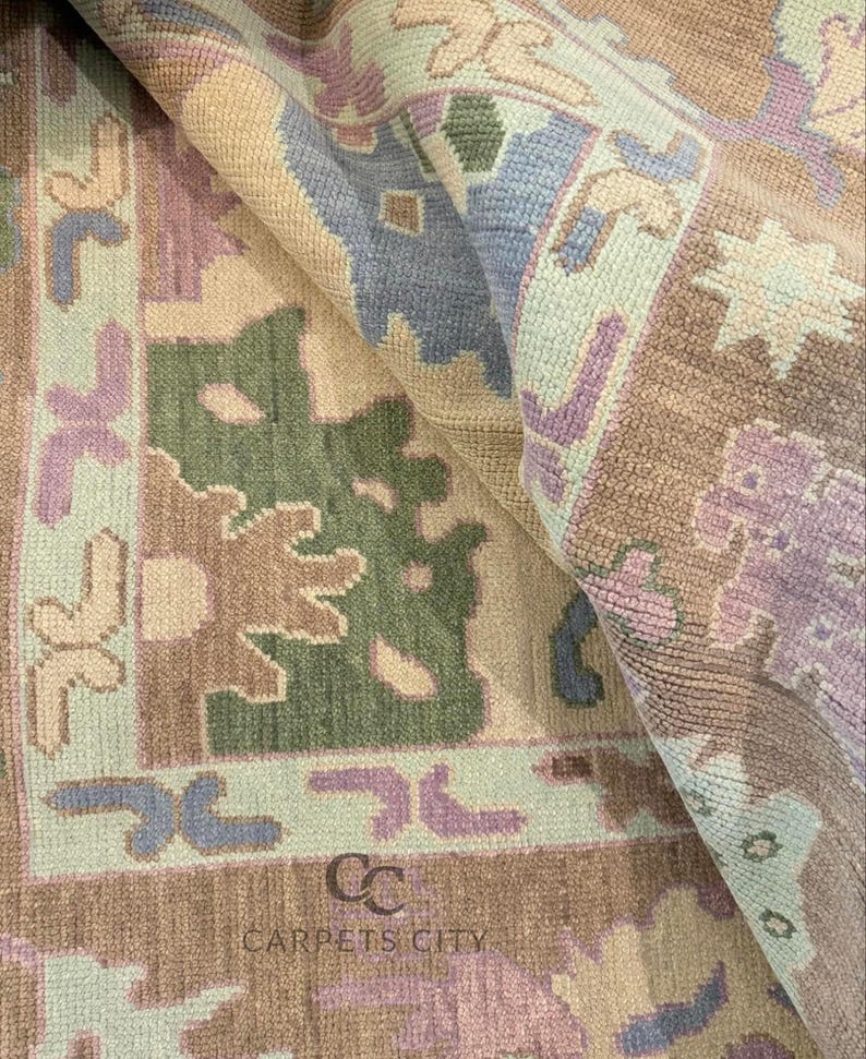 K&ouml;nnte beinhalten: Nahaufnahme eines gemusterten Teppichs in Beige-, Gr&uuml;n-, Lila- und Blaut&ouml;nen. Der Teppich zeigt ein geometrisches Design mit floralen und abstrakten Formen. Der Text "CARPETS CITY" ist sichtbar.