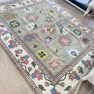May include: A rectangular rug with a light green central field and a floral pattern. The rug has a cream border with pink, blue, and green floral designs. The central field features large, stylized flowers in pink, blue, and white.