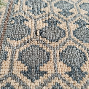 Handmade wool runner rug featuring a geometric lattice design in soft beige, blue, and green tones with tribal border details. This long hallway rug adds timeless style to entryways, kitchens, or bedside décor. Durable handwoven construction with fringe edges enhances farmhouse, boho, and modern interiors. Neutral yet colorful design makes it versatile for layering or as a statement runner. Perfect handmade rug for hallways, narrow spaces, and unique home décor accents.