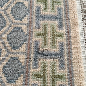 Handmade wool runner rug featuring a geometric lattice design in soft beige, blue, and green tones with tribal border details. This long hallway rug adds timeless style to entryways, kitchens, or bedside décor. Durable handwoven construction with fringe edges enhances farmhouse, boho, and modern interiors. Neutral yet colorful design makes it versatile for layering or as a statement runner. Perfect handmade rug for hallways, narrow spaces, and unique home décor accents.