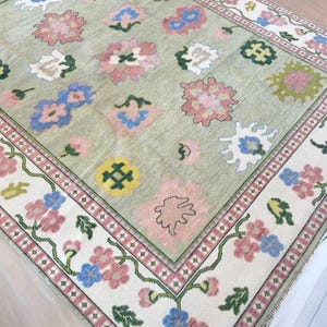 May include: A rectangular rug with a pale green central field and a floral pattern. The rug has a border with pink, blue, and white flowers on a cream background. The central design includes pink, blue, yellow, and white floral motifs.