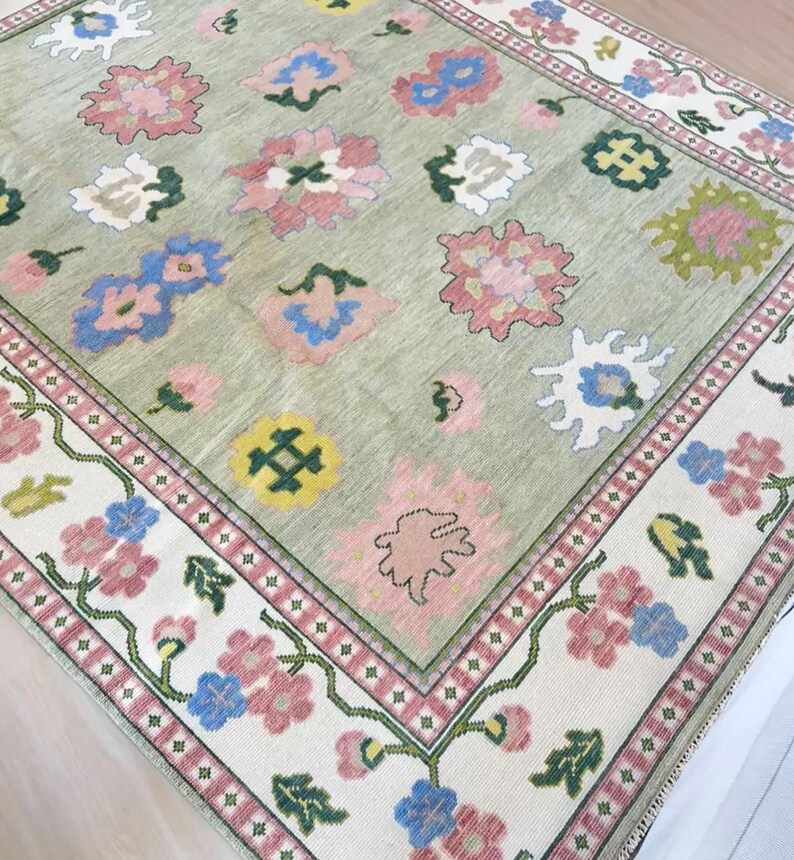 May include: A rectangular rug with a pale green central field and a floral pattern. The rug has a border with pink, blue, and white flowers on a cream background. The central design includes pink, blue, yellow, and white floral motifs.