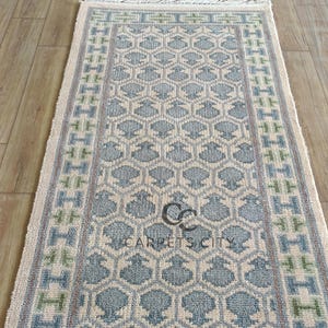 Handmade wool runner rug featuring a geometric lattice design in soft beige, blue, and green tones with tribal border details. This long hallway rug adds timeless style to entryways, kitchens, or bedside décor. Durable handwoven construction with fringe edges enhances farmhouse, boho, and modern interiors. Neutral yet colorful design makes it versatile for layering or as a statement runner. Perfect handmade rug for hallways, narrow spaces, and unique home décor accents.