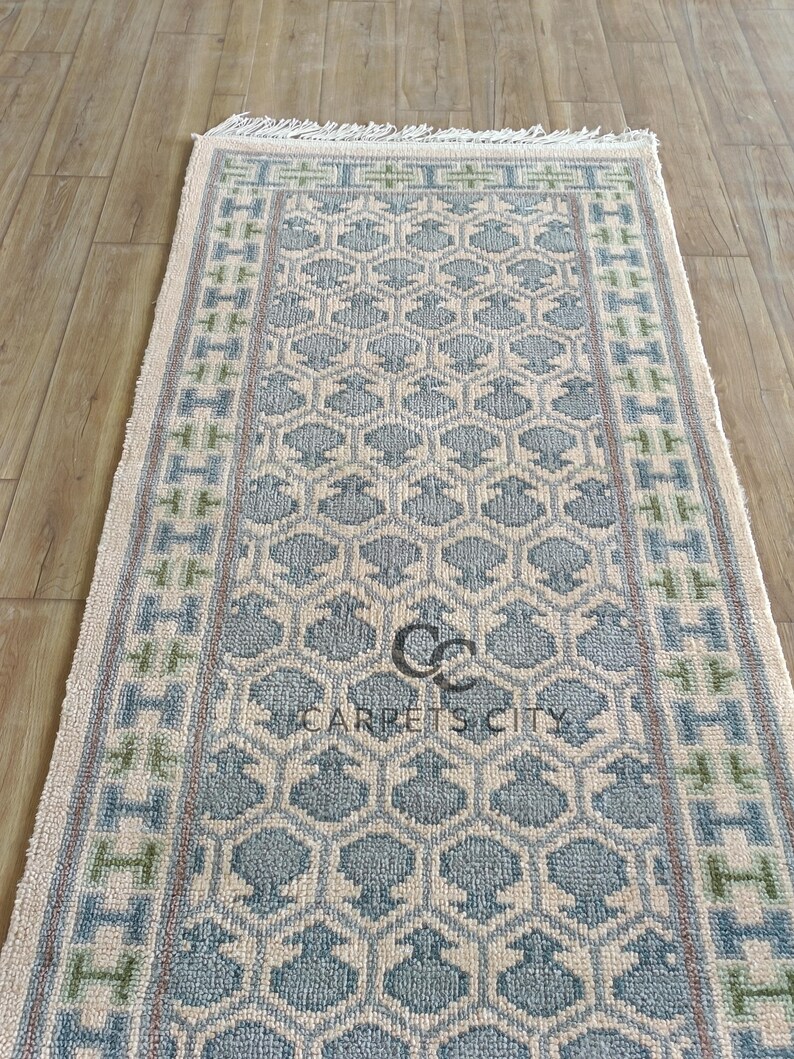Handmade wool runner rug featuring a geometric lattice design in soft beige, blue, and green tones with tribal border details. This long hallway rug adds timeless style to entryways, kitchens, or bedside décor. Durable handwoven construction with fringe edges enhances farmhouse, boho, and modern interiors. Neutral yet colorful design makes it versatile for layering or as a statement runner. Perfect handmade rug for hallways, narrow spaces, and unique home décor accents.