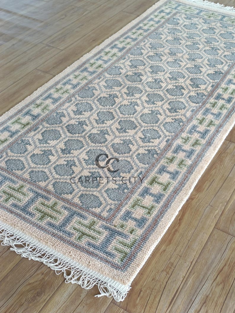 Handmade wool runner rug featuring a geometric lattice design in soft beige, blue, and green tones with tribal border details. This long hallway rug adds timeless style to entryways, kitchens, or bedside décor. Durable handwoven construction with fringe edges enhances farmhouse, boho, and modern interiors. Neutral yet colorful design makes it versatile for layering or as a statement runner. Perfect handmade rug for hallways, narrow spaces, and unique home décor accents.