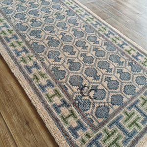 Handmade wool runner rug featuring a geometric lattice design in soft beige, blue, and green tones with tribal border details. This long hallway rug adds timeless style to entryways, kitchens, or bedside décor. Durable handwoven construction with fringe edges enhances farmhouse, boho, and modern interiors. Neutral yet colorful design makes it versatile for layering or as a statement runner. Perfect handmade rug for hallways, narrow spaces, and unique home décor accents.