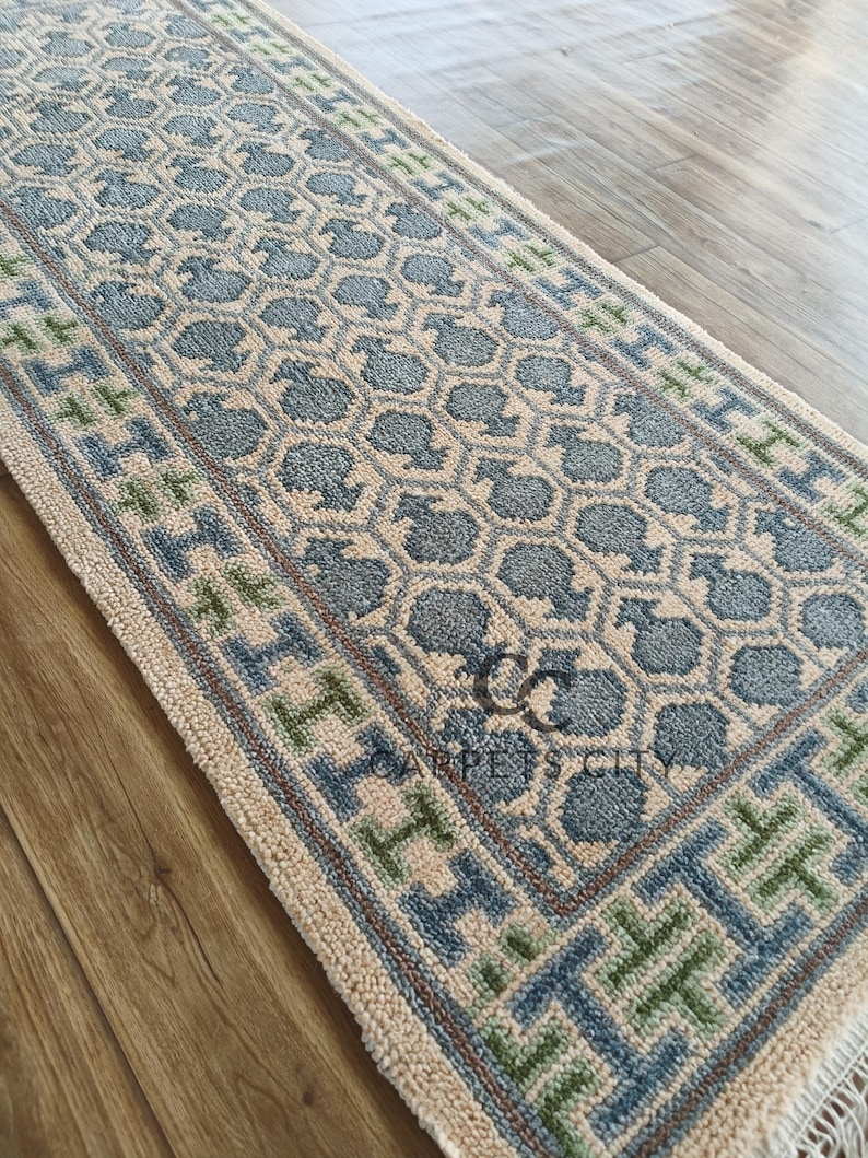 Handmade wool runner rug featuring a geometric lattice design in soft beige, blue, and green tones with tribal border details. This long hallway rug adds timeless style to entryways, kitchens, or bedside décor. Durable handwoven construction with fringe edges enhances farmhouse, boho, and modern interiors. Neutral yet colorful design makes it versatile for layering or as a statement runner. Perfect handmade rug for hallways, narrow spaces, and unique home décor accents.