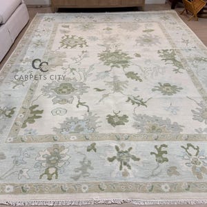 May include: Large rectangular area rug with a floral pattern in shades of cream, green, and blue. The rug features a central design surrounded by a border. The text "CARPETS CITY" is visible in the corner.
