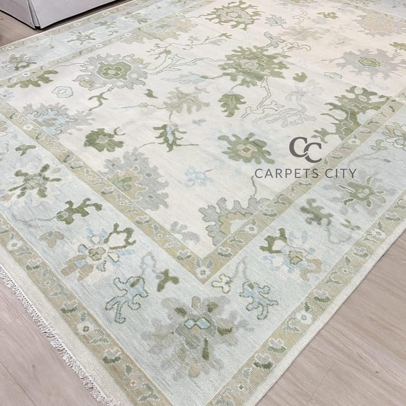 May include: A large, rectangular area rug with a floral pattern in shades of cream, green, and gray. The rug features a central design with a border. The text "CARPETS CITY" is visible on the rug.