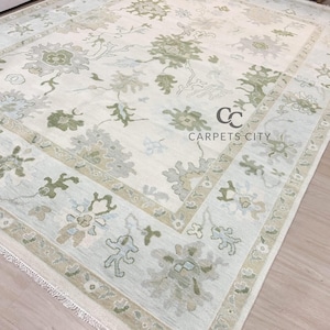 May include: A rectangular area rug with a floral pattern in shades of green, gray, and beige on an off-white background. The rug has a border with floral motifs and the text "CARPETS CITY".