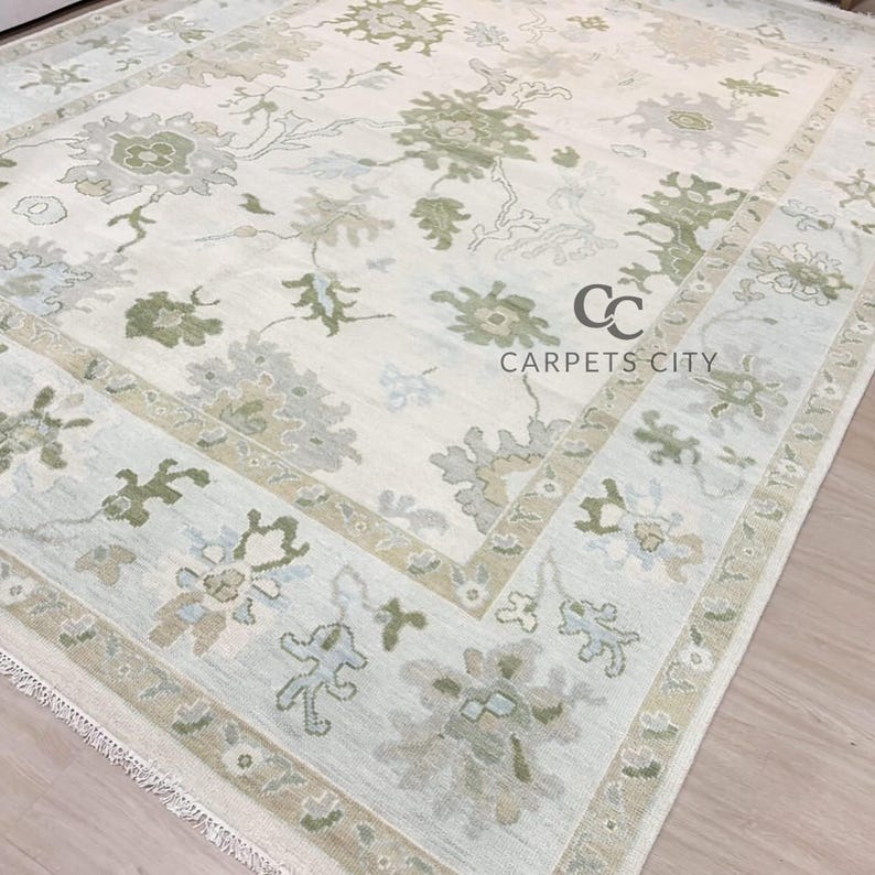 May include: A rectangular area rug with a floral pattern in shades of green, gray, and beige on an off-white background. The rug has a border with floral motifs and the text "CARPETS CITY".