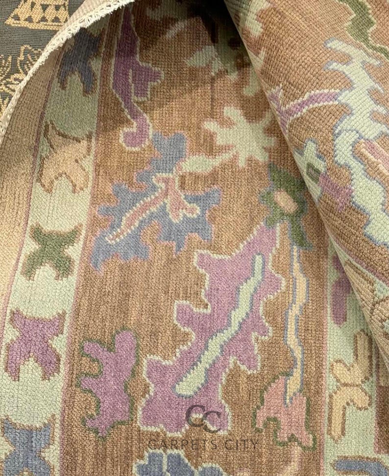 K&ouml;nnte beinhalten: Gerollter Teppich mit sich wiederholendem Blumenmuster in Braun-, Lila-, Blau- und Gr&uuml;nt&ouml;nen. Der Teppich hat ein weiches, strukturiertes Aussehen. Der Text "CARPETS CITY" ist sichtbar.