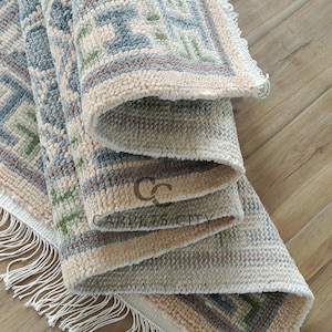 Handmade wool runner rug featuring a geometric lattice design in soft beige, blue, and green tones with tribal border details. This long hallway rug adds timeless style to entryways, kitchens, or bedside décor. Durable handwoven construction with fringe edges enhances farmhouse, boho, and modern interiors. Neutral yet colorful design makes it versatile for layering or as a statement runner. Perfect handmade rug for hallways, narrow spaces, and unique home décor accents.