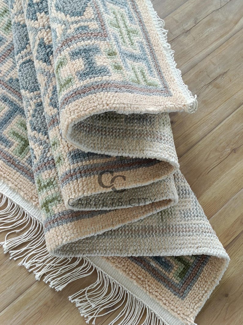 Handmade wool runner rug featuring a geometric lattice design in soft beige, blue, and green tones with tribal border details. This long hallway rug adds timeless style to entryways, kitchens, or bedside décor. Durable handwoven construction with fringe edges enhances farmhouse, boho, and modern interiors. Neutral yet colorful design makes it versatile for layering or as a statement runner. Perfect handmade rug for hallways, narrow spaces, and unique home décor accents.