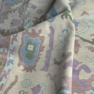 K&ouml;nnte beinhalten: Beiger Teppich mit detailliertem Muster in Blau-, Lila-, Gr&uuml;n- und Braunt&ouml;nen. Der Teppich weist ein sich wiederholendes Blumen- und geometrisches Design auf, mit dem Text "CARPETS CITY" sichtbar.