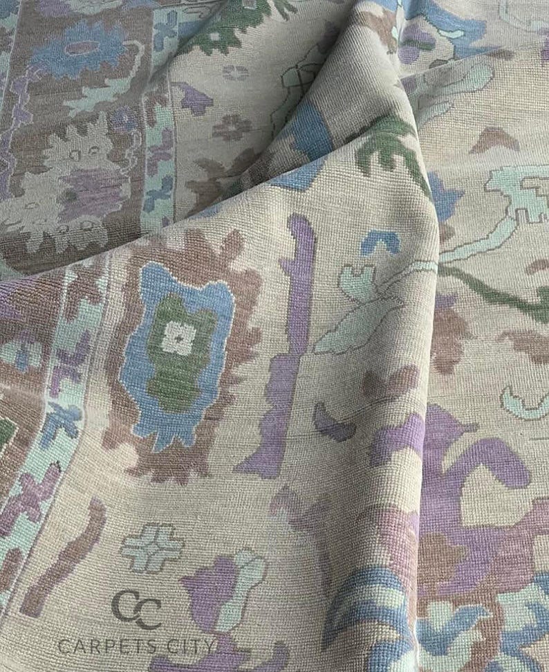 K&ouml;nnte beinhalten: Beiger Teppich mit detailliertem Muster in Blau-, Lila-, Gr&uuml;n- und Braunt&ouml;nen. Der Teppich weist ein sich wiederholendes Blumen- und geometrisches Design auf, mit dem Text "CARPETS CITY" sichtbar.