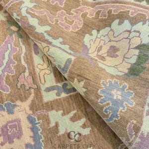 K&ouml;nnte beinhalten: Nahaufnahme eines aufgerollten Teppichs mit detailliertem Blumenmuster. Der Teppich hat eine Farbpalette aus Braun, Hellblau, Lavendel und Gr&uuml;n. Der Text "CARPETS CITY" ist auf dem Teppich zu sehen.