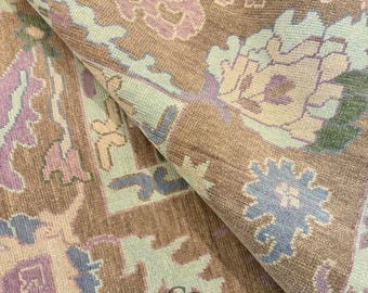 Könnte beinhalten: Nahaufnahme eines aufgerollten Teppichs mit detailliertem Blumenmuster. Der Teppich hat eine Farbpalette aus Braun, Hellblau, Lavendel und Grün. Der Text "CARPETS CITY" ist auf dem Teppich zu sehen.