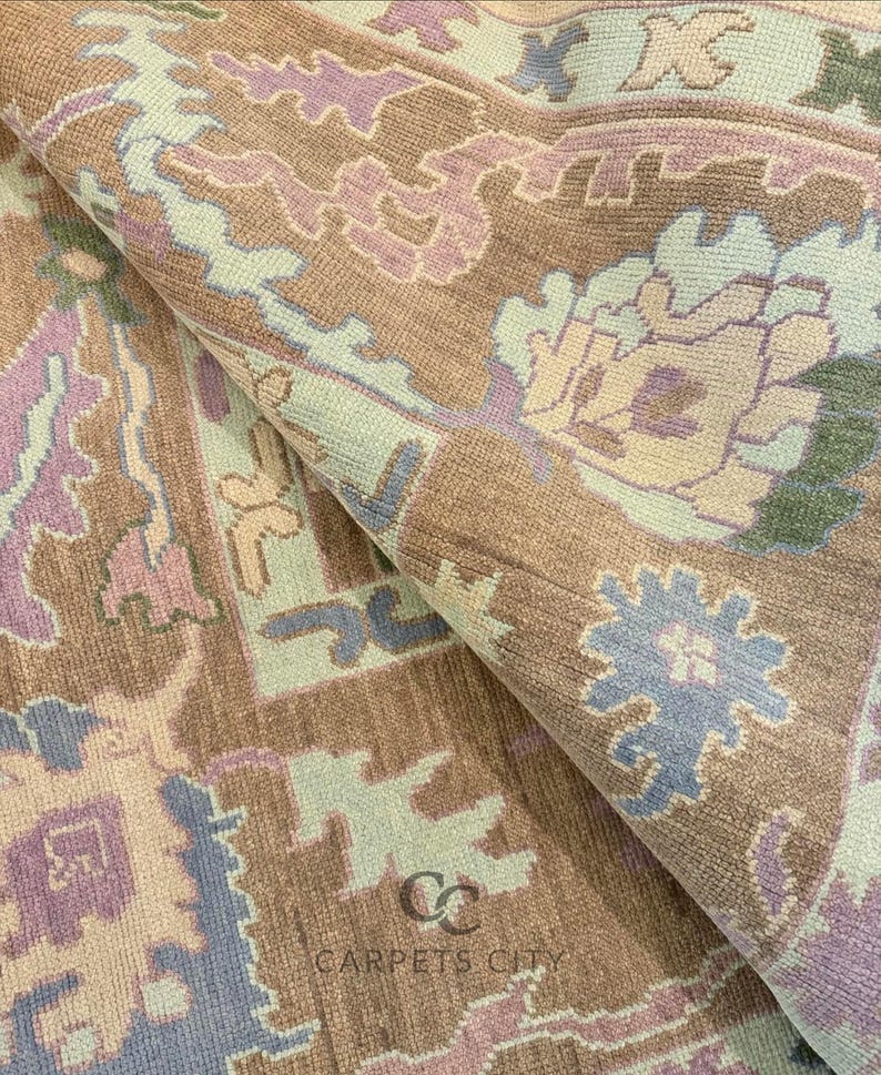 K&ouml;nnte beinhalten: Nahaufnahme eines aufgerollten Teppichs mit detailliertem Blumenmuster. Der Teppich hat eine Farbpalette aus Braun, Hellblau, Lavendel und Gr&uuml;n. Der Text "CARPETS CITY" ist auf dem Teppich zu sehen.