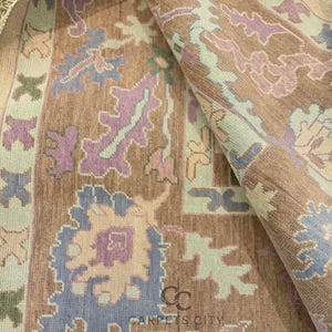 K&ouml;nnte beinhalten: Eine aufgerollte Teppichfl&auml;che mit einem detaillierten Blumenmuster in Braun-, Lila-, Blau- und Gr&uuml;nt&ouml;nen. Der Teppich tr&auml;gt unten den Text "CARPETS CITY". Das Design umfasst stilisierte Blumen- und geometrische Formen.