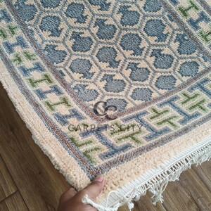Handmade wool runner rug featuring a geometric lattice design in soft beige, blue, and green tones with tribal border details. This long hallway rug adds timeless style to entryways, kitchens, or bedside décor. Durable handwoven construction with fringe edges enhances farmhouse, boho, and modern interiors. Neutral yet colorful design makes it versatile for layering or as a statement runner. Perfect handmade rug for hallways, narrow spaces, and unique home décor accents.