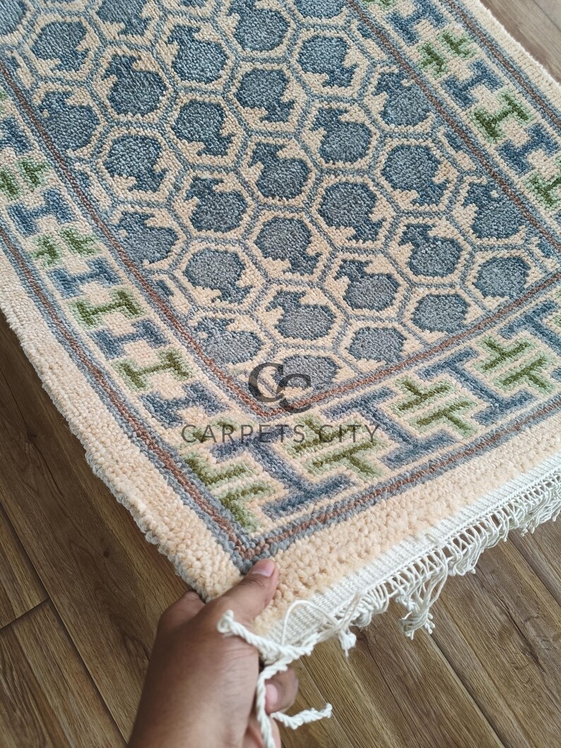 Handmade wool runner rug featuring a geometric lattice design in soft beige, blue, and green tones with tribal border details. This long hallway rug adds timeless style to entryways, kitchens, or bedside décor. Durable handwoven construction with fringe edges enhances farmhouse, boho, and modern interiors. Neutral yet colorful design makes it versatile for layering or as a statement runner. Perfect handmade rug for hallways, narrow spaces, and unique home décor accents.