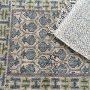 Handmade wool runner rug featuring a geometric lattice design in soft beige, blue, and green tones with tribal border details. This long hallway rug adds timeless style to entryways, kitchens, or bedside décor. Durable handwoven construction with fringe edges enhances farmhouse, boho, and modern interiors. Neutral yet colorful design makes it versatile for layering or as a statement runner. Perfect handmade rug for hallways, narrow spaces, and unique home décor accents.