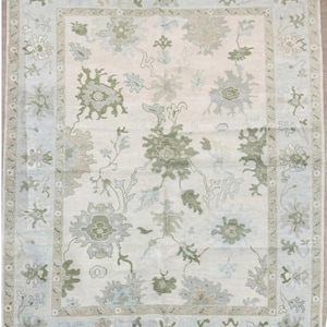 May include: A rectangular area rug with a cream-colored central field and a light blue border. The rug features a floral pattern in shades of green and gray, with a detailed border design. The rug is suitable for living rooms and bedrooms.