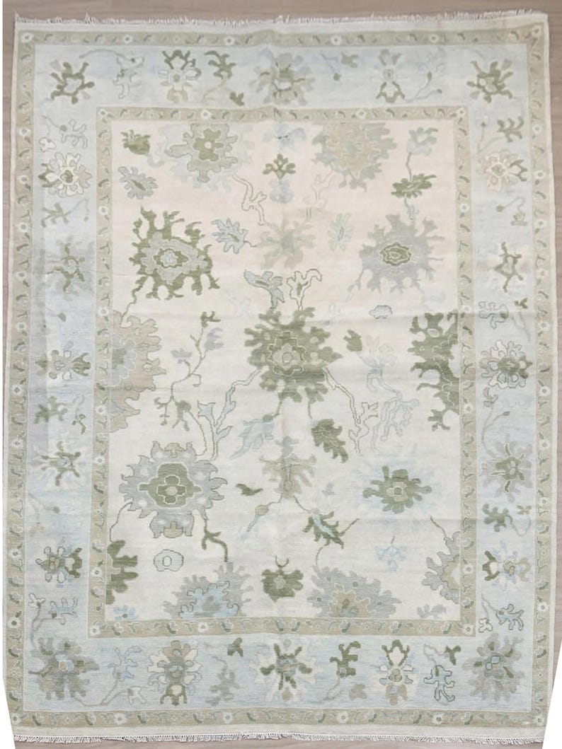 May include: A rectangular area rug with a cream-colored central field and a light blue border. The rug features a floral pattern in shades of green and gray, with a detailed border design. The rug is suitable for living rooms and bedrooms.