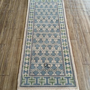 Handmade wool runner rug featuring a geometric lattice design in soft beige, blue, and green tones with tribal border details. This long hallway rug adds timeless style to entryways, kitchens, or bedside décor. Durable handwoven construction with fringe edges enhances farmhouse, boho, and modern interiors. Neutral yet colorful design makes it versatile for layering or as a statement runner. Perfect handmade rug for hallways, narrow spaces, and unique home décor accents.