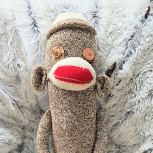 May include: A handmade sock monkey doll in shades of brown and cream. The monkey has a red mouth, button eyes, and decorative accents. The doll is approximately 18 inches tall.