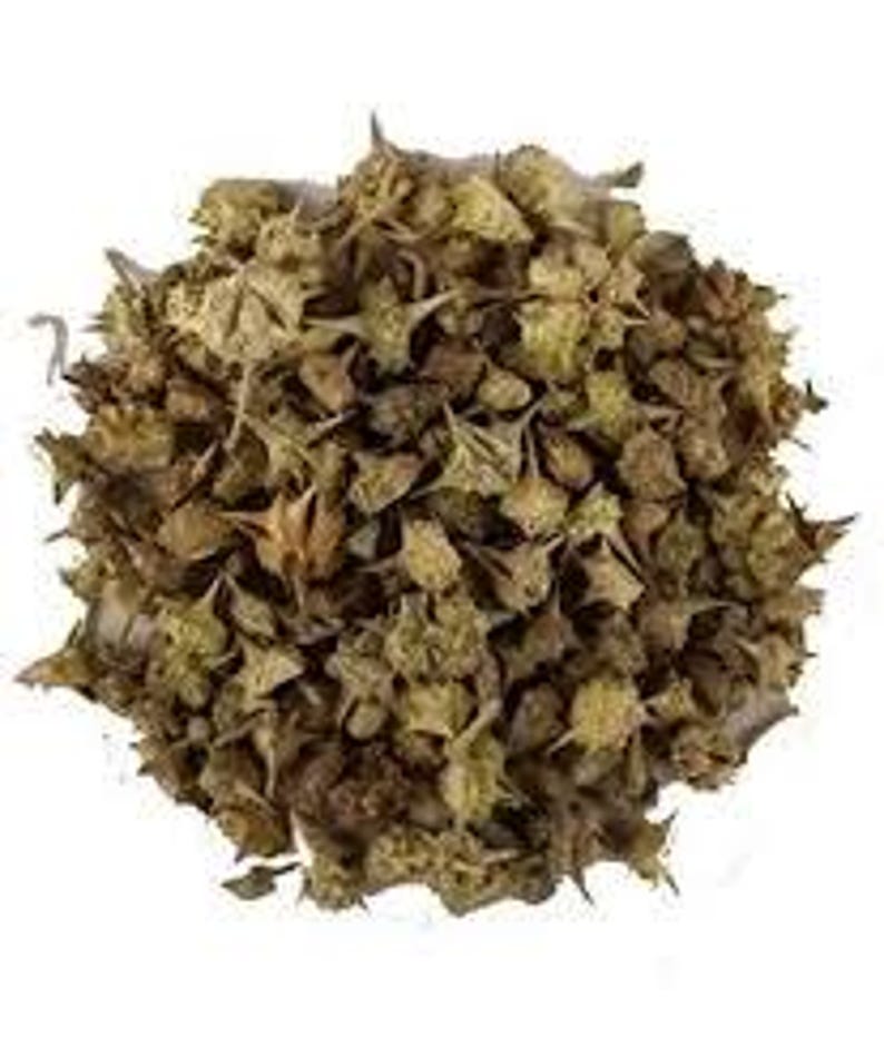 May include: A pile of dried, tan-colored Tribulus Terrestris plant parts, featuring spiky seed pods and small leaves. The image is a close-up shot against a white background, highlighting the texture and details of the plant material.
