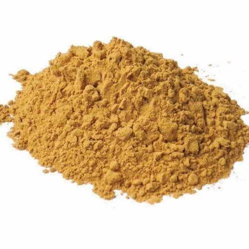 May include: A pile of light brown powder against a white background. The powder has a coarse, granular texture and appears to be a spice or ingredient used in cooking or baking. The color is a warm, earthy tone.