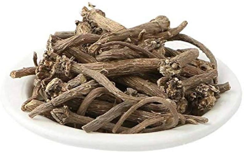 May include: A white ceramic bowl filled with dried, brown, root-like pieces. The pieces have a rough texture and varying lengths, with some curved and others straight. The image is well-lit, highlighting the natural colors and textures of the contents.