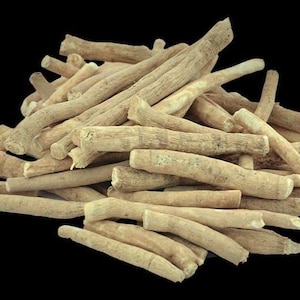 May include: A pile of ashwagandha root pieces, light tan in color, against a black background. The roots are cylindrical and have a rough, textured appearance. The image highlights the natural form of the herbal product.