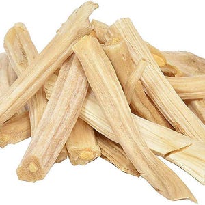 May include: A pile of light brown Palo Santo wood sticks. The sticks are rectangular with a natural, textured appearance. The ends of the sticks are cut, revealing the wood's grain. The wood has a light, natural color.